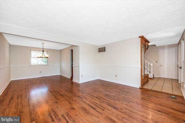 unfurnished living room featuring an inviting chandelier, dark hardwood / wood-style flooring, and a textured ceiling