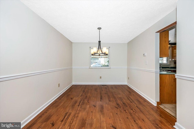 unfurnished dining area featuring an inviting chandelier, dark hardwood / wood-style flooring, and a textured ceiling