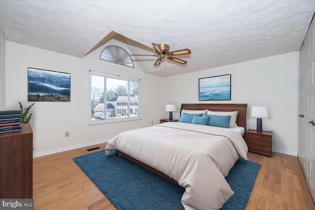 bedroom with light hardwood / wood-style floors, lofted ceiling, ceiling fan, and a textured ceiling