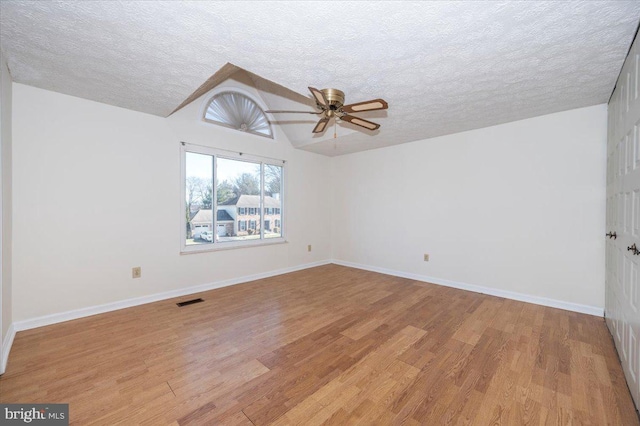 empty room with ceiling fan, light wood-type flooring, vaulted ceiling, and a textured ceiling