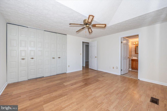 unfurnished bedroom with light wood-type flooring, a closet, ensuite bathroom, and a textured ceiling