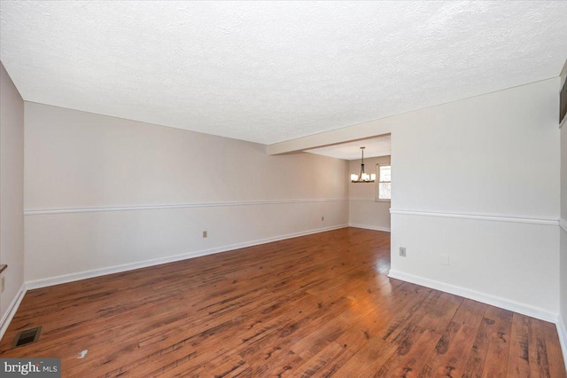 unfurnished room with dark hardwood / wood-style floors, a textured ceiling, and an inviting chandelier