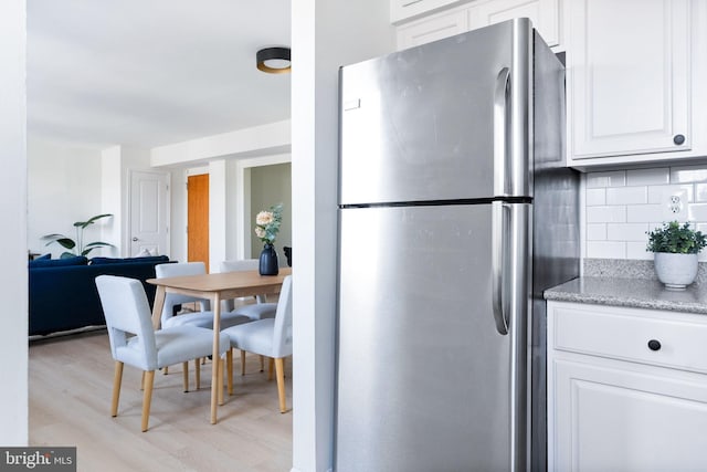 kitchen featuring stainless steel refrigerator, white cabinetry, light wood-type flooring, and backsplash