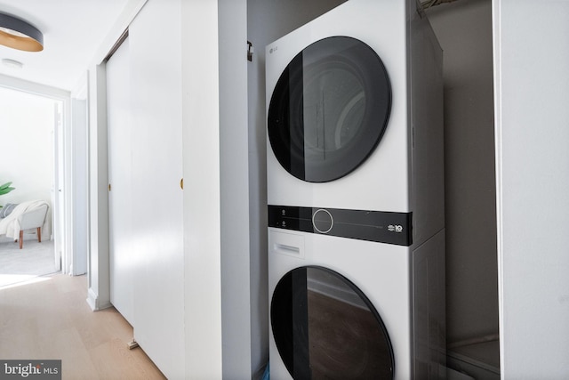 clothes washing area featuring light wood-type flooring and stacked washing maching and dryer