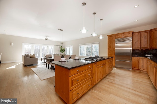 kitchen featuring appliances with stainless steel finishes, a kitchen island, pendant lighting, dark stone counters, and light hardwood / wood-style floors