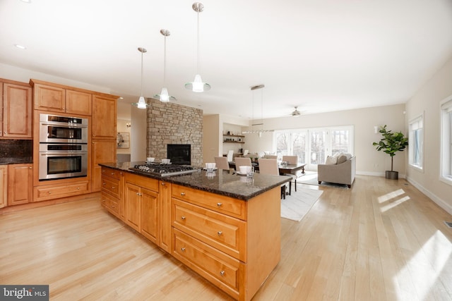 kitchen with decorative light fixtures, light wood-type flooring, dark stone counters, and appliances with stainless steel finishes