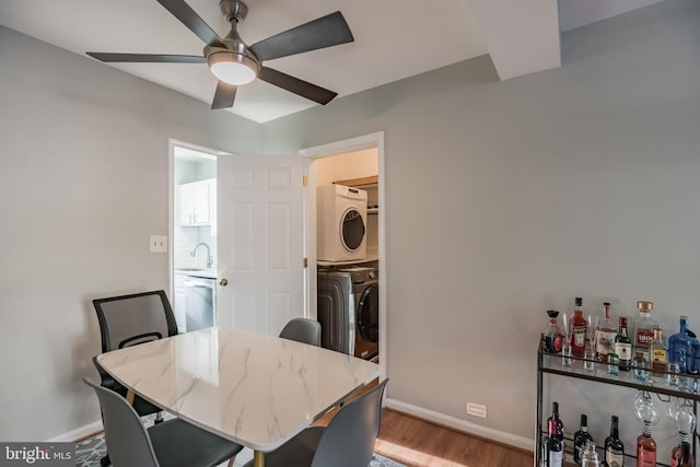 dining room featuring sink, light hardwood / wood-style flooring, stacked washer and clothes dryer, and ceiling fan