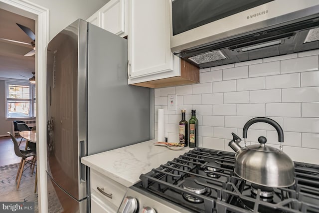 kitchen with appliances with stainless steel finishes, tasteful backsplash, white cabinetry, ceiling fan, and light stone countertops