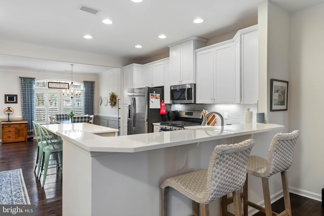 kitchen with appliances with stainless steel finishes, white cabinetry, hanging light fixtures, kitchen peninsula, and dark wood-type flooring