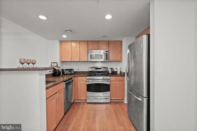 kitchen featuring stainless steel appliances, kitchen peninsula, light hardwood / wood-style floors, and dark stone counters