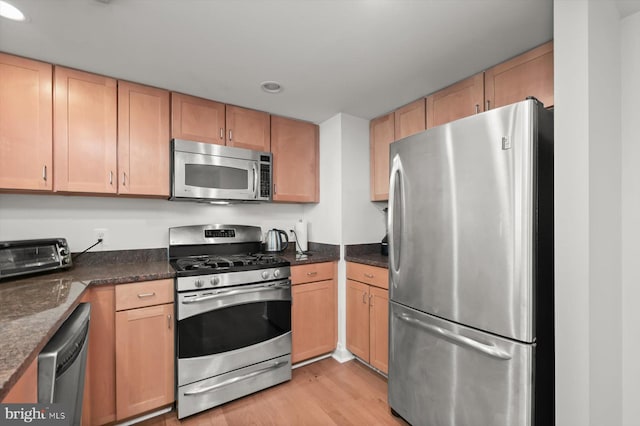 kitchen featuring dark stone countertops, light hardwood / wood-style flooring, and appliances with stainless steel finishes