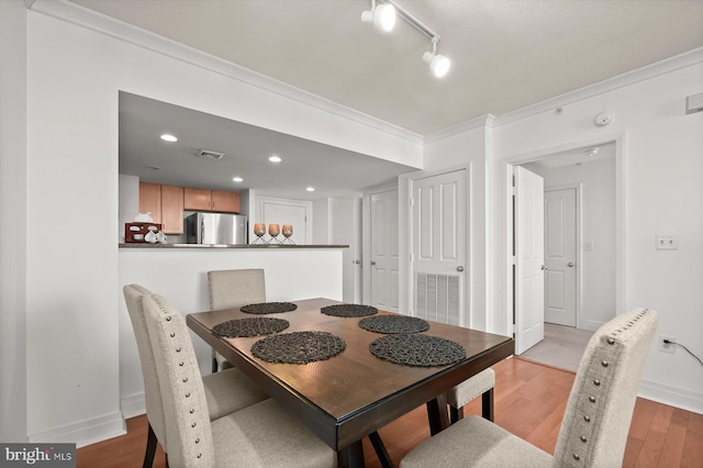 dining room with crown molding, light hardwood / wood-style floors, and rail lighting