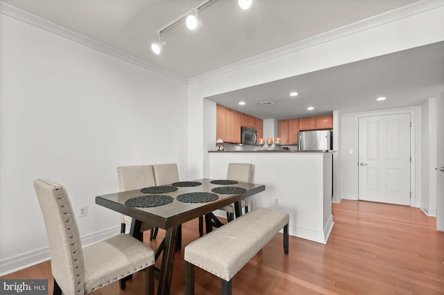 dining room with ornamental molding, rail lighting, and light hardwood / wood-style floors