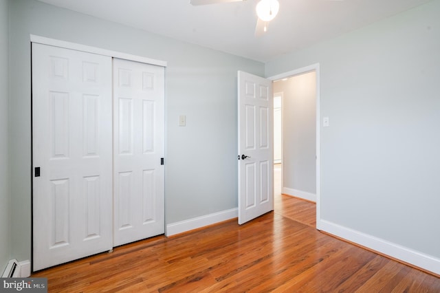 unfurnished bedroom featuring ceiling fan, wood-type flooring, a baseboard radiator, and a closet