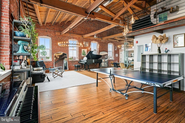 game room with brick wall, hardwood / wood-style floors, high vaulted ceiling, beamed ceiling, and a chandelier