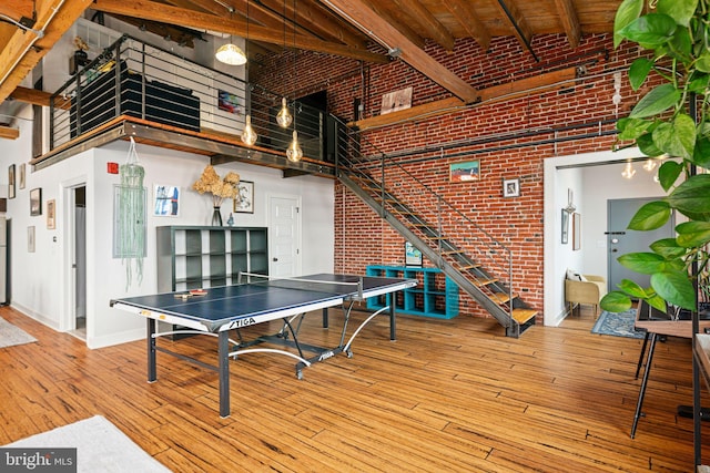 playroom with brick wall, a towering ceiling, and hardwood / wood-style floors