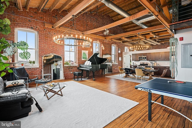 interior space featuring beam ceiling, a towering ceiling, electric panel, brick wall, and light wood-type flooring