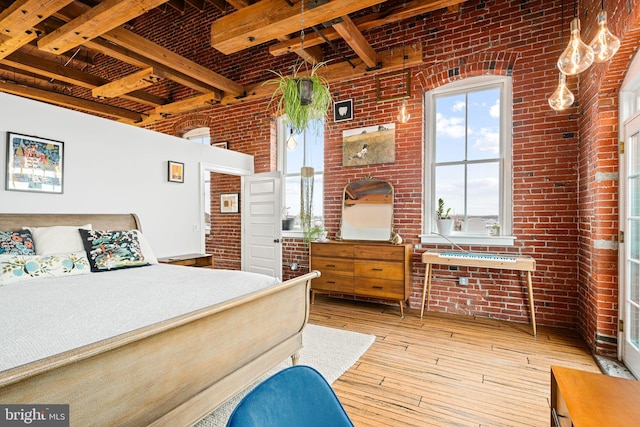 bedroom featuring beamed ceiling, brick wall, and light hardwood / wood-style flooring