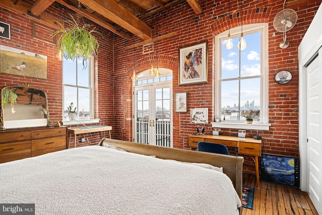 bedroom featuring beamed ceiling, brick wall, hardwood / wood-style flooring, and french doors