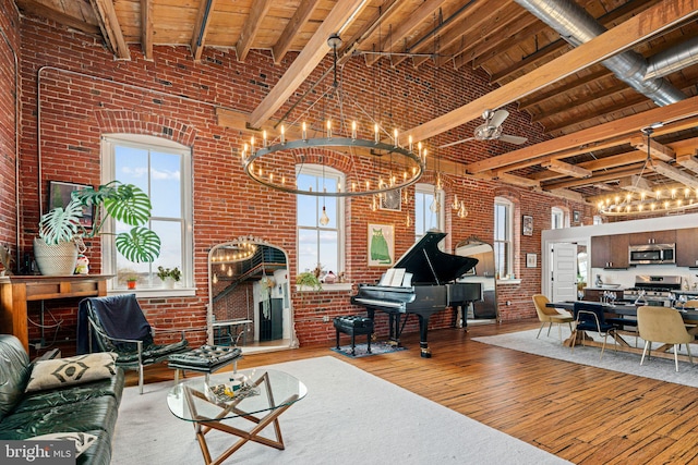 living room with brick wall, a fireplace, wood-type flooring, a high ceiling, and beam ceiling