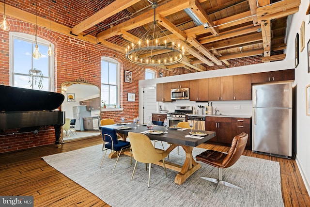 dining area featuring sink, beam ceiling, a notable chandelier, brick wall, and dark hardwood / wood-style flooring