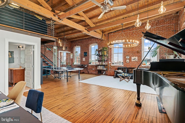 interior space with brick wall, ceiling fan with notable chandelier, beamed ceiling, wood-type flooring, and wood ceiling