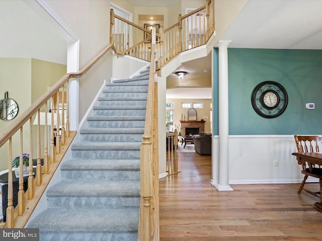 6852 Fielding Ct, Frederick, MD 21703 - staircase with a brick fireplace, wood finished floors, a high ceiling, ornate columns, and a wainscoted wall