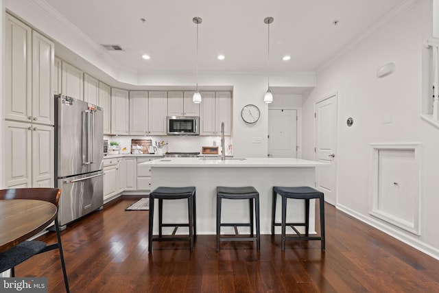 kitchen with ornamental molding, stainless steel appliances, decorative light fixtures, and an island with sink