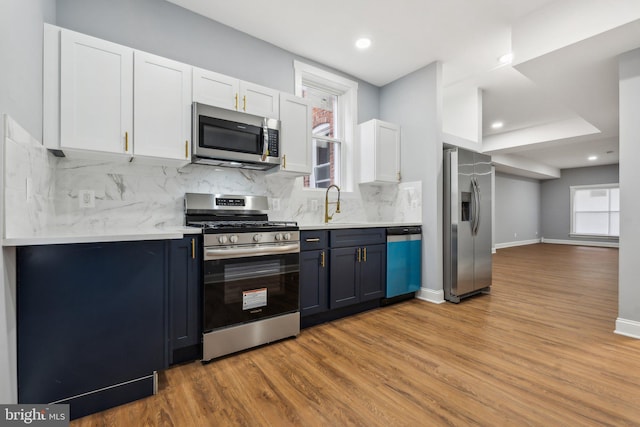 kitchen with stainless steel appliances, white cabinetry, blue cabinetry, and decorative backsplash