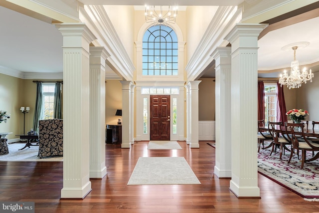 entrance foyer featuring decorative columns, dark hardwood / wood-style floors, a wealth of natural light, and a notable chandelier