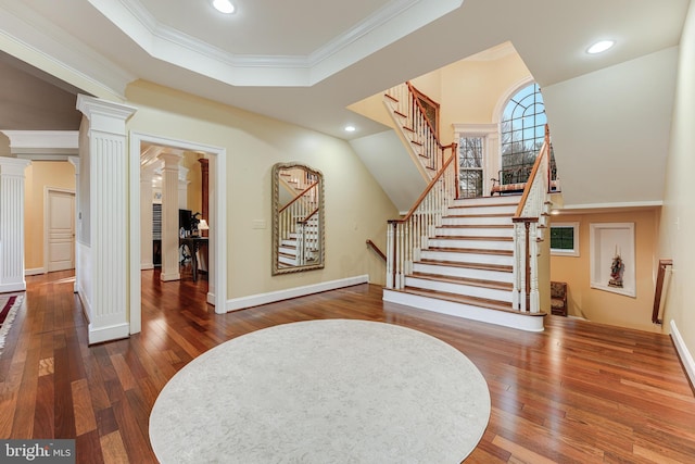 entryway featuring crown molding, wood-type flooring, a tray ceiling, and decorative columns