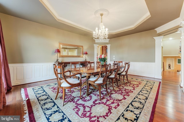 dining area with a tray ceiling, decorative columns, and hardwood / wood-style floors