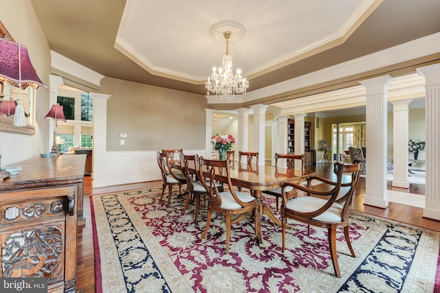 dining room with ornate columns, a raised ceiling, wood-type flooring, and a notable chandelier