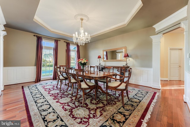 dining area featuring hardwood / wood-style flooring, a raised ceiling, and decorative columns