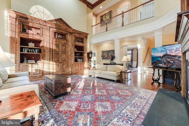 living room with hardwood / wood-style flooring, built in features, decorative columns, a high ceiling, and ornamental molding