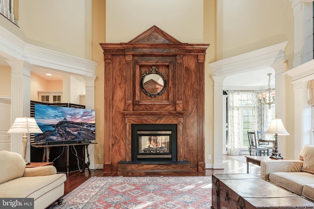 living room with a multi sided fireplace, a towering ceiling, decorative columns, a chandelier, and hardwood / wood-style flooring