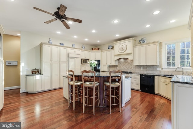 kitchen featuring sink, a breakfast bar area, custom exhaust hood, built in appliances, and a center island