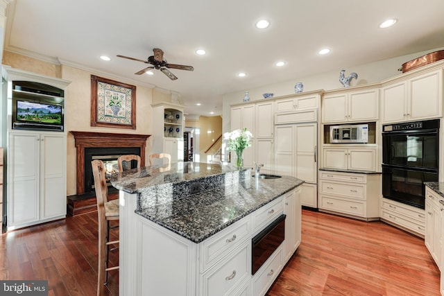 kitchen with dark stone countertops, black double oven, an island with sink, and a kitchen bar