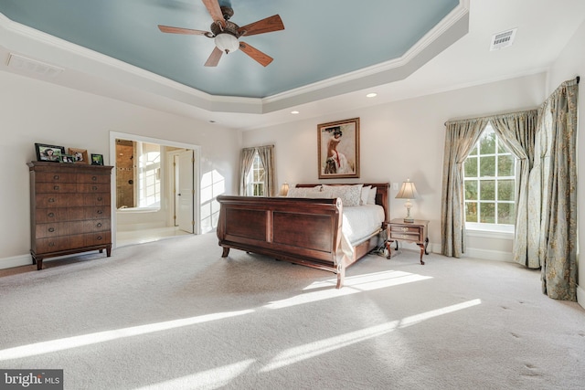 bedroom with connected bathroom, ornamental molding, light colored carpet, and a raised ceiling