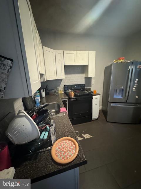 kitchen with white cabinets, backsplash, dark tile patterned floors, stainless steel refrigerator with ice dispenser, and black electric range