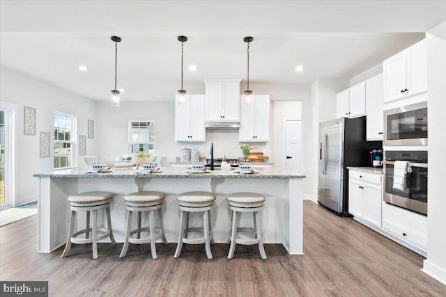 kitchen with stainless steel appliances, decorative light fixtures, a center island with sink, and white cabinetry