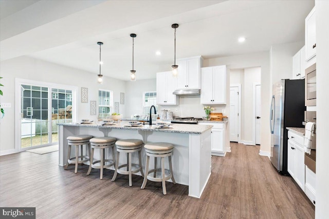 kitchen with a kitchen island with sink, white cabinetry, pendant lighting, and light stone counters