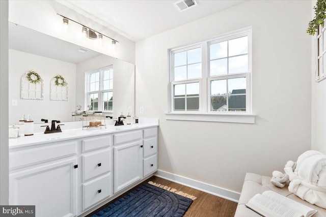 full bathroom with a sink, wood finished floors, visible vents, baseboards, and double vanity