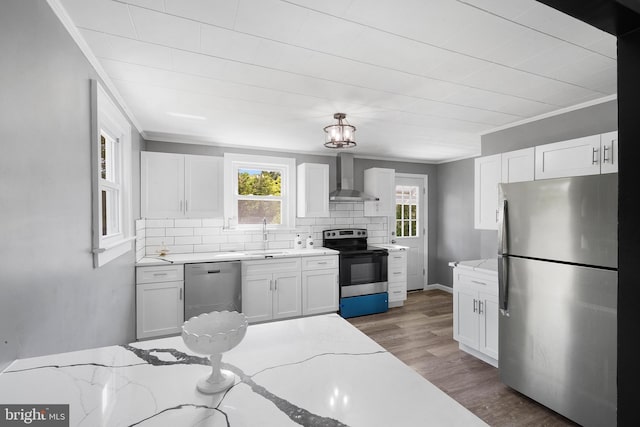 kitchen with wall chimney exhaust hood, stainless steel appliances, light stone counters, and white cabinets