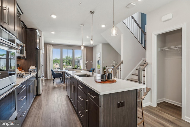 kitchen with stainless steel appliances, dark brown cabinets, sink, and a center island with sink