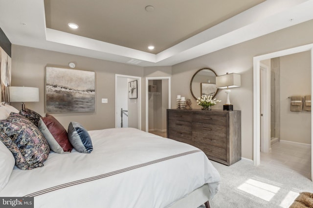 bedroom with light colored carpet, ensuite bath, and a tray ceiling