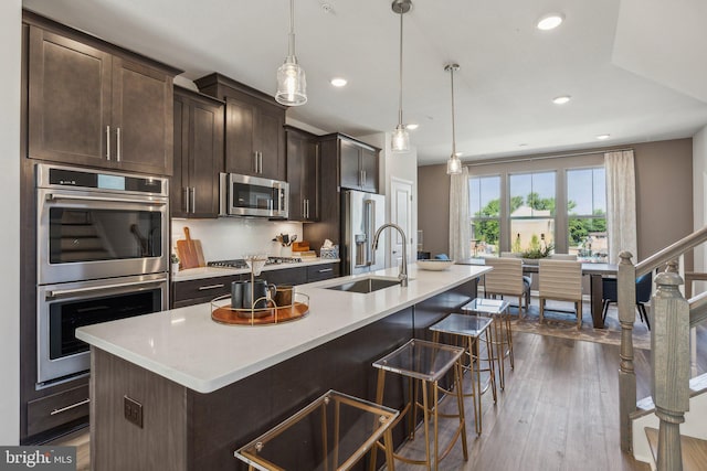 kitchen with sink, a kitchen island with sink, stainless steel appliances, a kitchen bar, and decorative light fixtures