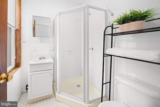 bathroom featuring vanity, toilet, a shower with door, and tile walls