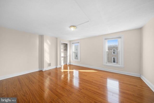 unfurnished room with built in shelves and light wood-type flooring