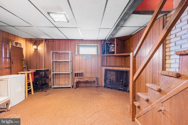 basement featuring a fireplace, a paneled ceiling, wood walls, and carpet flooring